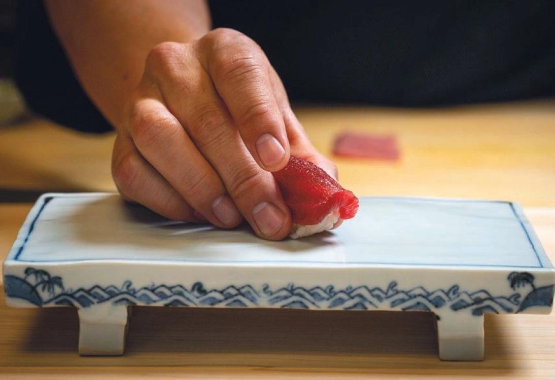 Chef placing nigiri on a blue-and-white rectangular ceramic presentation plate.