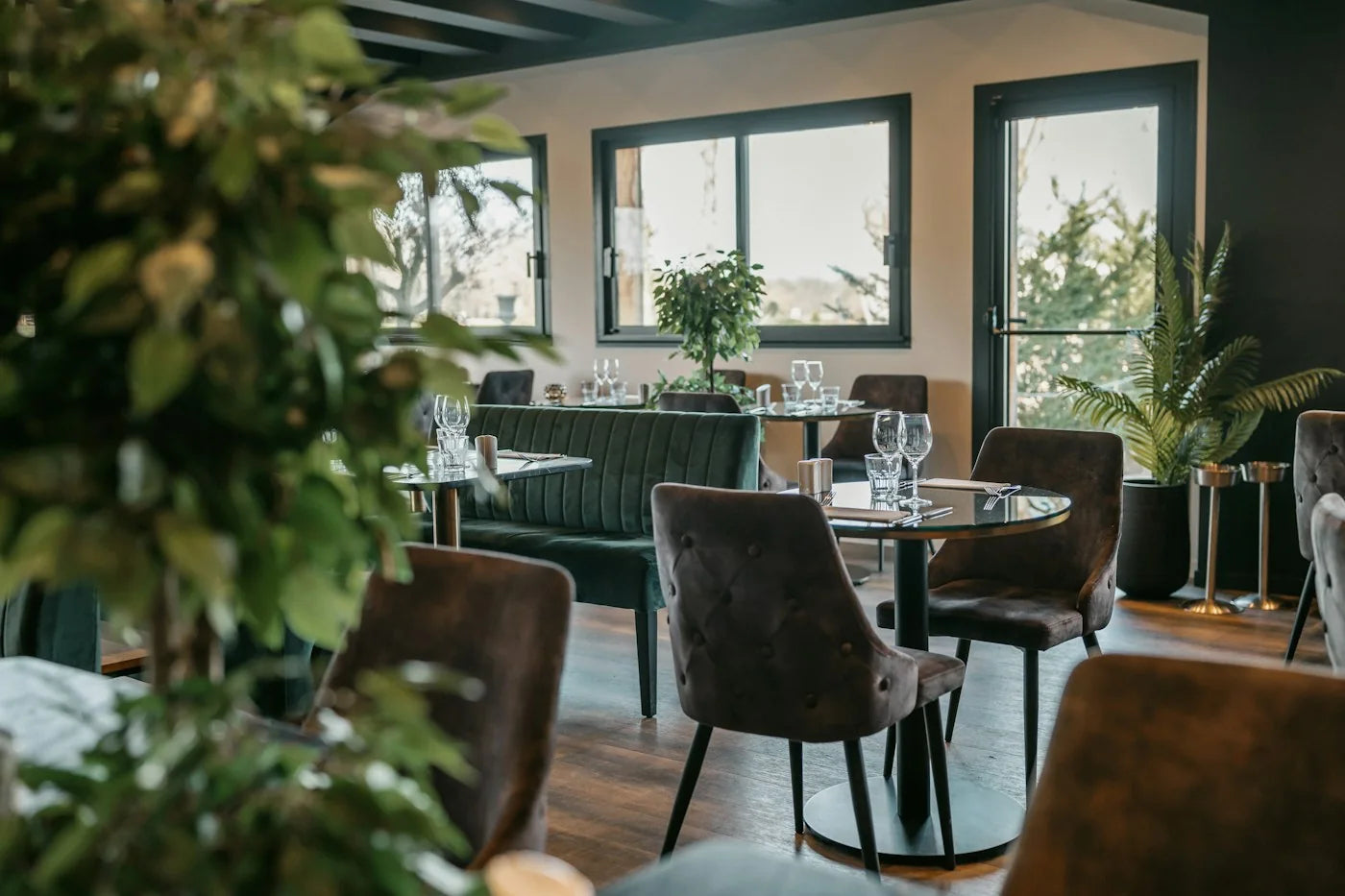 Upholstered chairs, a green banquette and round pedestal tables in a furnished restaurant