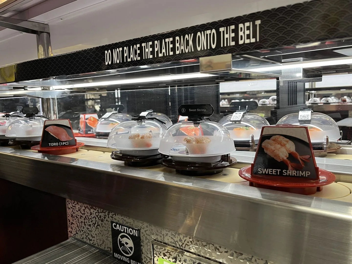 Covered plates on a continuous sushi conveyor · Kura Revolving Sushi Bar