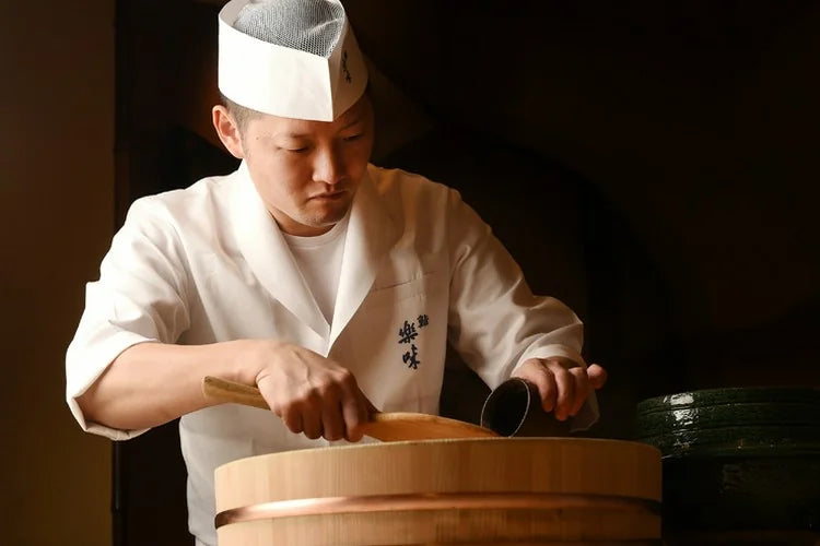 Chef handling sushi rice in a wooden hangiri behind a sushi counter