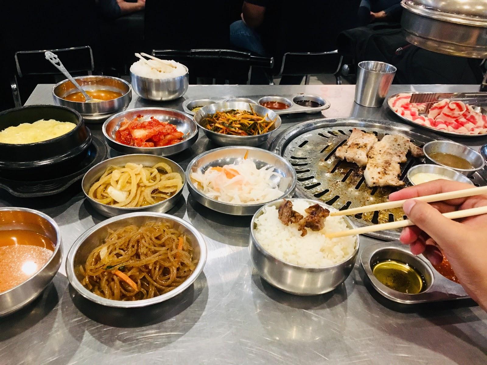 Korean BBQ service with a tabletop grill, meat, banchan, rice, soup and shared dishes