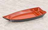 Black and red boat-shaped melamine serving plate with divider on a stone tabletop
