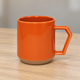 C011 orange mug with tan base on a wooden table
