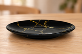 K210-LIT1 black and gold ceramic plate on a light wood table