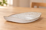 MA311-WK ivory speckled leaf-shaped ceramic plate on a light wood table