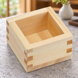 OMS-101 wooden sake masu cup on a light stone dining table, showing the plain interior