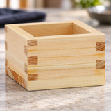 OMS-103 wooden sake masu cup on a pale restaurant table, shown from the lower front view