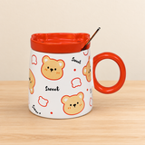PC54-1 bear-print mug with orange lid and spoon on a pale wood tabletop