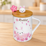 PC62-1 rabbit and blossom mug with rabbit-knob lid and flower spoon on a pale wood tabletop