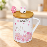PC62-2 rabbit and blossom mug with rabbit-knob lid and flower spoon on a pale wood tabletop