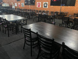 Black metal restaurant chair with black padded seat; restaurant setting with other furniture illustrative