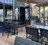 Black Stackable Indoor/Outdoor Chair with Black Aluminum Frame in a restaurant setting; other furniture is illustrative