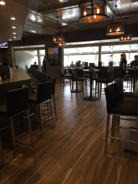 Black Upholstered Restaurant Barstool with Stainless Steel Legs in a restaurant setting; other furniture is illustrative