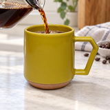 Mustard ceramic mug with angular handle being filled with coffee