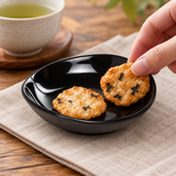 Black shallow melamine dish serving rice crackers at tea time
