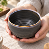 K537-BW dark ceramic matcha bowl held for inspection; whisk and table accessories illustrative, bowl sold separately.