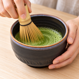 K537-BW dark ceramic matcha bowl during matcha whisking; whisk and table accessories illustrative, bowl sold separately.