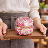 Pink floral tea container in a carrying setting. Contextual accessories are not included.