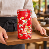 Tall red floral tea container in a carrying setting. Contextual accessories are not included.
