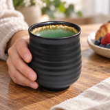AS70-EM black ribbed ceramic teacup with green interior in a hand-held breakfast setting; contextual accessories not included.