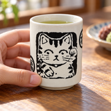 Black beckoning-cat ceramic teacup in a table setting. Contextual accessories are not included.