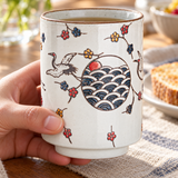 FDC1 crane and wave ceramic teacup in a hand-held breakfast setting; contextual accessories not included.