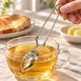 HST013 closed stainless steel tea infuser tongs lowered into tea; cup and tabletop props illustrative.