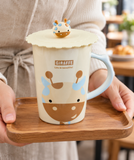 Cream giraffe mug with scalloped lid and giraffe knob in a carrying setting. Contextual accessories are not included.