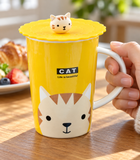 Yellow cat mug with scalloped lid and cat knob in a breakfast setting. Contextual accessories are not included.