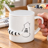 Sitting-cat white mug with lid, spoon and raised striped tail in a breakfast setting. Contextual accessories are not included.
