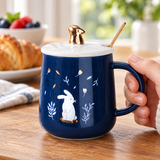 Navy rabbit mug with white lid, gold-tone knob and spoon in a breakfast setting. Contextual accessories are not included.
