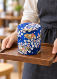 Blue blossom-and-fan tea container in a carrying setting. Contextual accessories are not included.