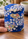 Blue blossom-and-fan tea container in a table setting. Contextual accessories are not included.
