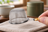 6592-70 small stainless-steel tea strainer held inverted by its short bamboo grip; contextual cup and linen not included.