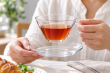 HARIO CSW-1T wide glass cup lifted above its matching glass saucer; tea and table accessories are contextual.