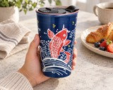 SM12-6728 red-koi tumbler held at a breakfast table with its original black lid seated.