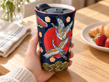 SM12-7007 crane-pattern tumbler held at a breakfast table with its original black lid seated.