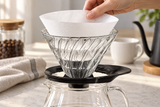Placing a paper filter into the HARIO VDGR-02-B glass dripper; server and other accessories are contextual.