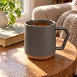 Gray ceramic C001GY mug filled with tea on a reading table beside a book