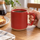 Red ceramic C001RD mug with angular handle and unglazed base held beside breakfast