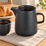 Black ceramic coffee server on a breakfast table beside a cup