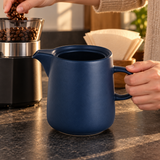 Navy ceramic coffee server being positioned beside a grinder during coffee preparation