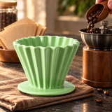 Green fluted ceramic coffee dripper beside a hand grinder being filled with coffee beans