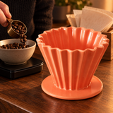 Orange fluted ceramic coffee dripper beside coffee beans being measured for brewing