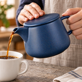 Navy coffee dripper pot pouring coffee with its flat lid held in place; cups and other props not included.
