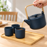 Navy teapot pouring tea into a matching cup on the wooden tray