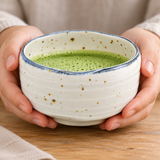 White blue-rim bowl cradled in hands with prepared matcha