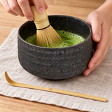 Dark charcoal matcha set during whisking with bamboo scoop alongside
