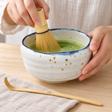 White blue-rim matcha set during whisking with bamboo scoop alongside