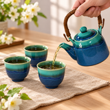 Blue-green teapot pouring tea into a matching cup with two more cups alongside